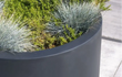 Adezz Circum polyester plantenbak rond recht in grijs gevuld met groene beplanting op een terras.