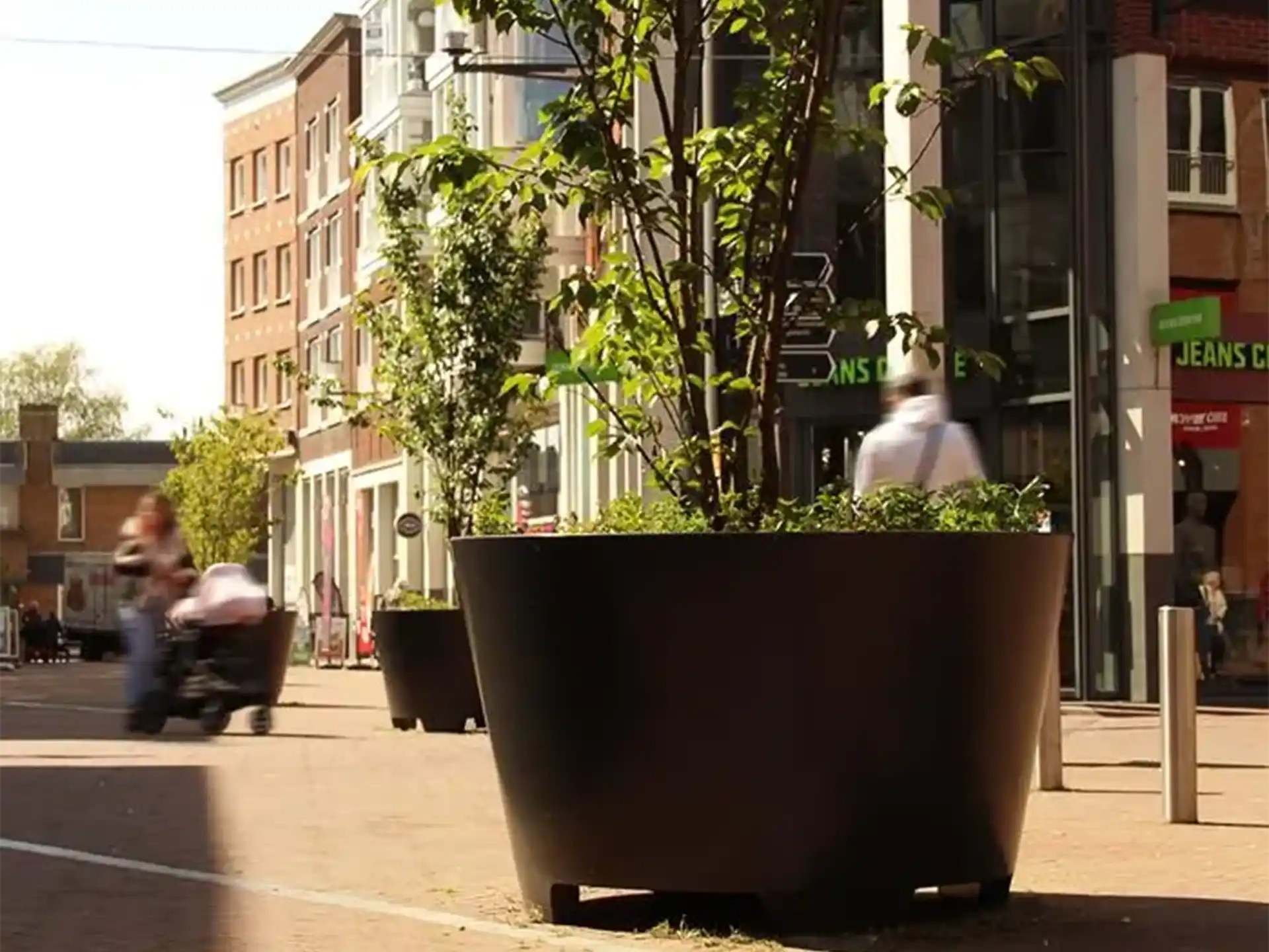 Adezz Conic aluminium plantenbak met poten en beplanting in een winkelstraat met stedelijke omgeving.
