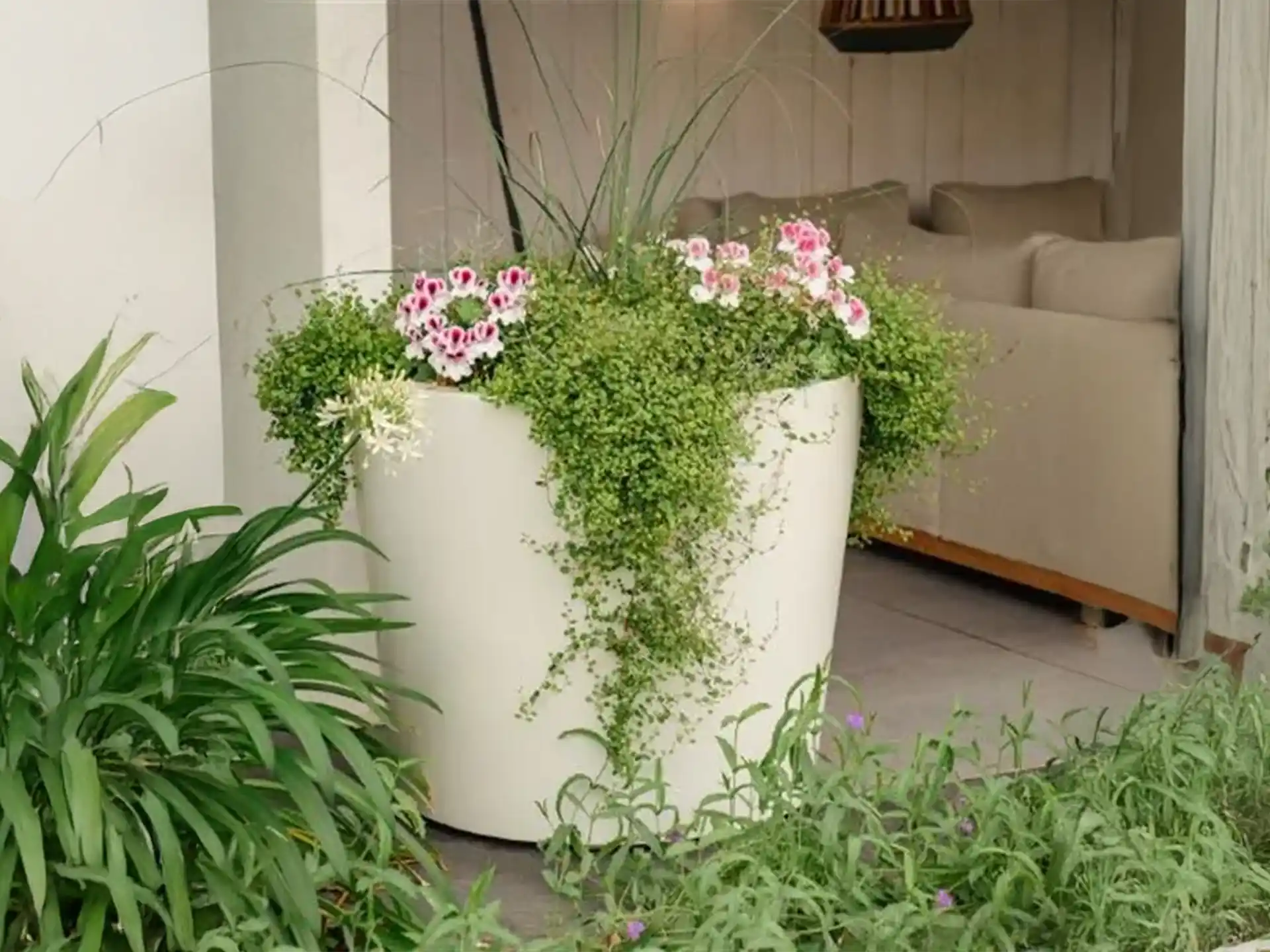 Adezz Conic polyester plantenbak rond schuin in het wit met groene planten en bloemen bij een terras.