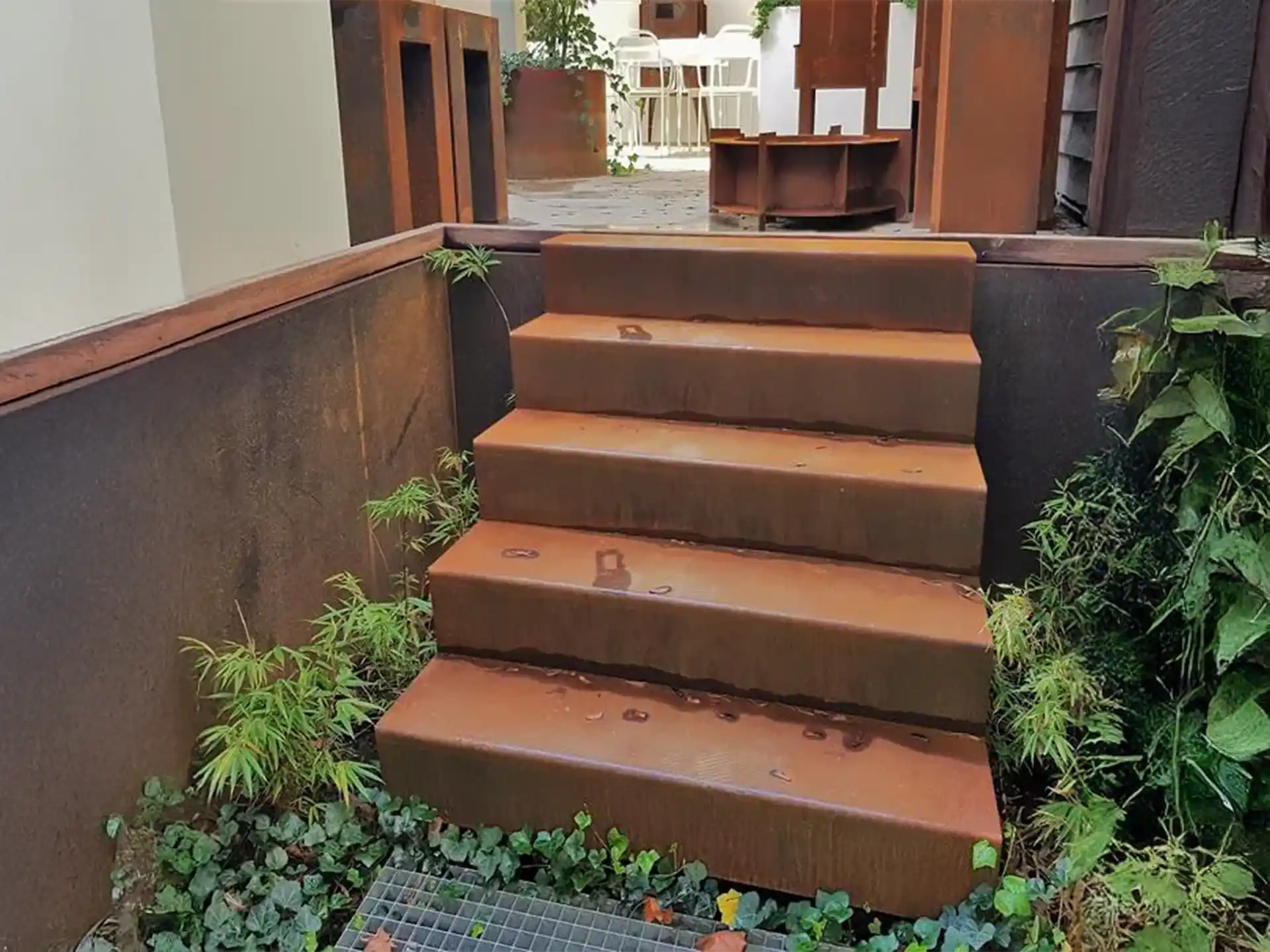 Adezz kant en klare trap van cortenstaal met natuurlijke roestkleur, geplaatst in een groene tuinomgeving met beplanting langs de randen.