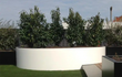 Grote witte Adezz Ellipse aluminium plantenbak in een tuin met meerdere groene bomen en strak gazon.
