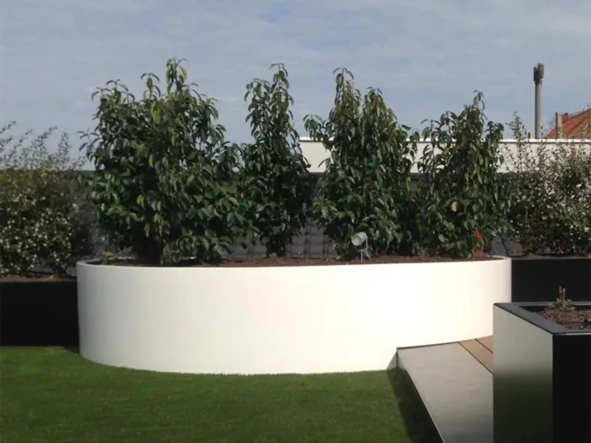 Grote witte Adezz Ellipse aluminium plantenbak in een tuin met meerdere groene bomen en strak gazon.