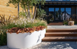 Witte Adezz Ellipse aluminium plantenbak in een moderne voortuin met siergrassen en bloeiende planten.