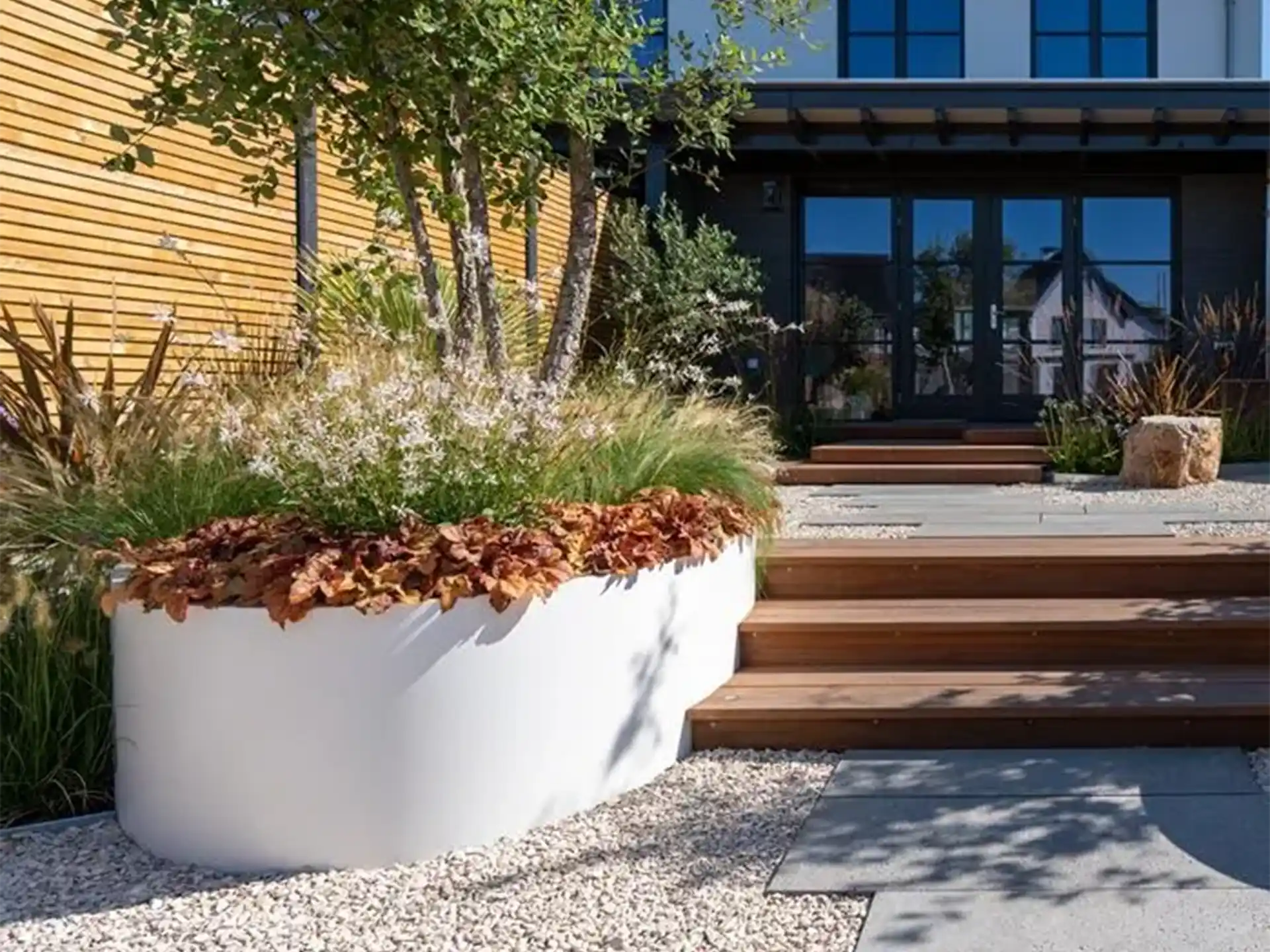Witte Adezz Ellipse aluminium plantenbak in een moderne voortuin met siergrassen en bloeiende planten.