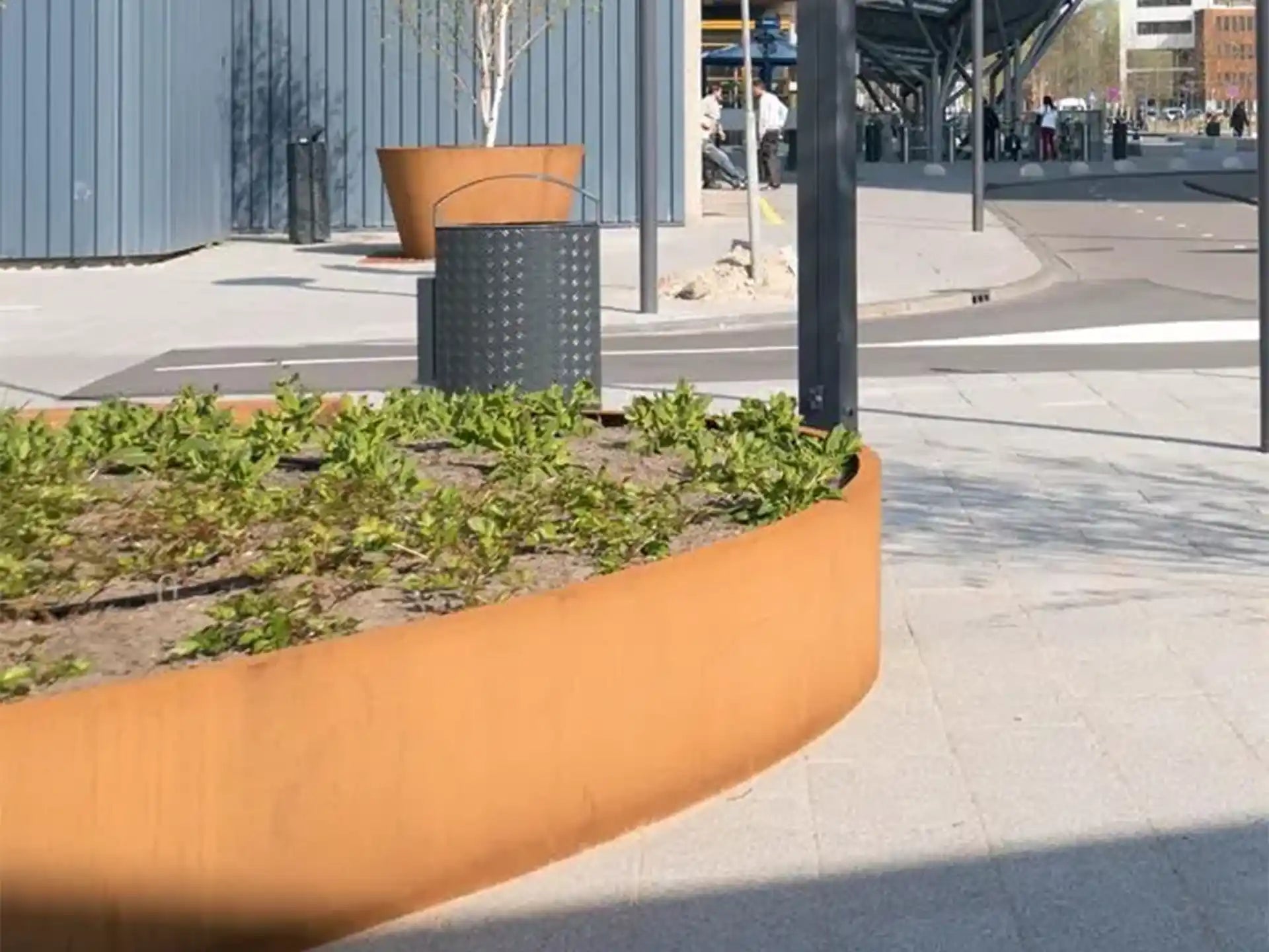 Adezz Ellipse Cortenstaal Plantenbak Ovaal met bodem, beplant met lage groene planten op een modern stadsplein.