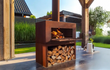 Adezz Forno Enok tuinhaard cortenstaal, sfeervolle buitenhaard met brandend vuur en houtopslag, geplaatst op modern terras.