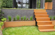 Moderne tuin met een Adezz kant en klare trap van cortenstaal en bijpassende plantenbak, stijlvol geïntegreerd in een verhoogd terras.