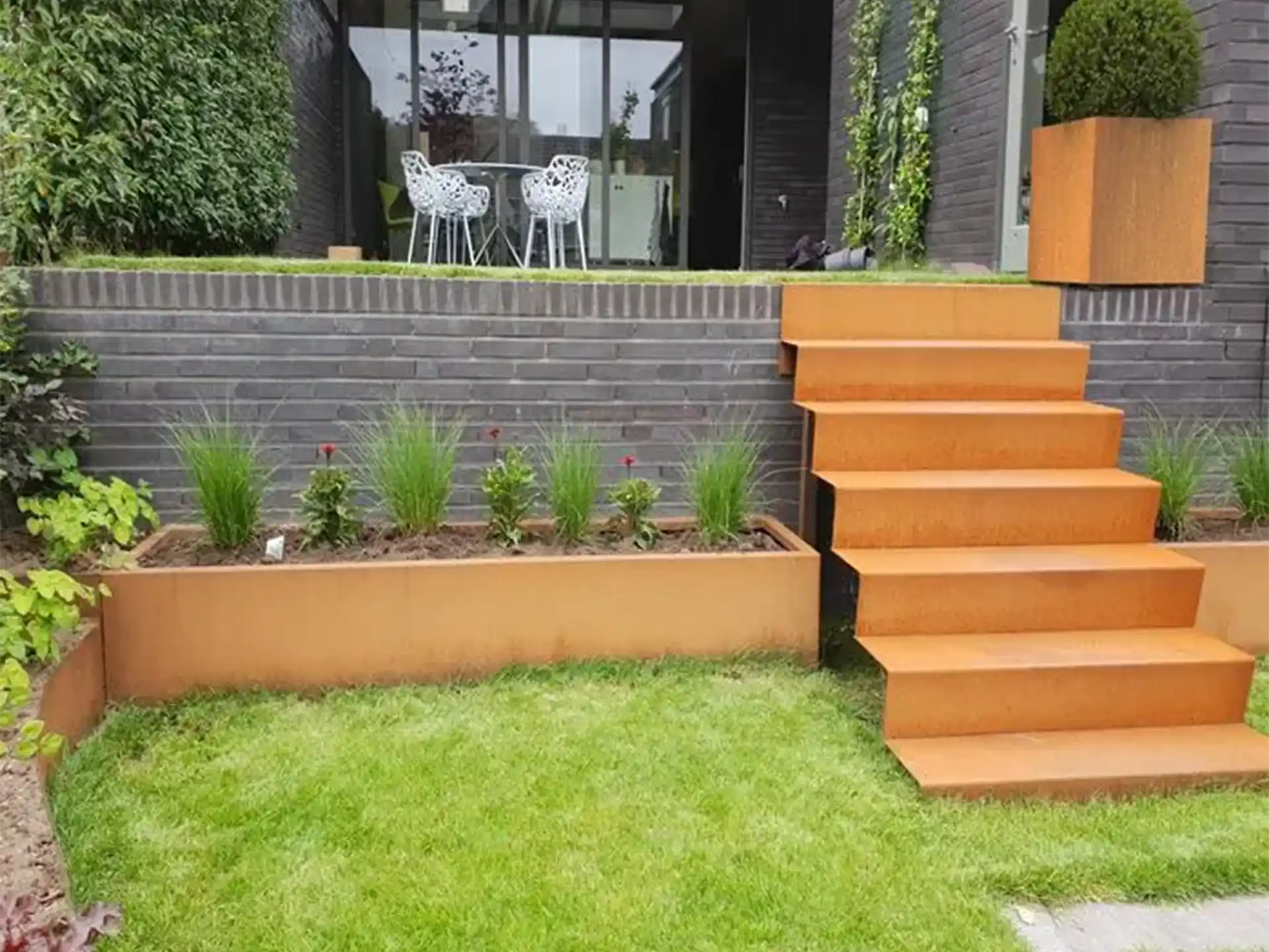Moderne tuin met een Adezz kant en klare trap van cortenstaal en bijpassende plantenbak, stijlvol geïntegreerd in een verhoogd terras.