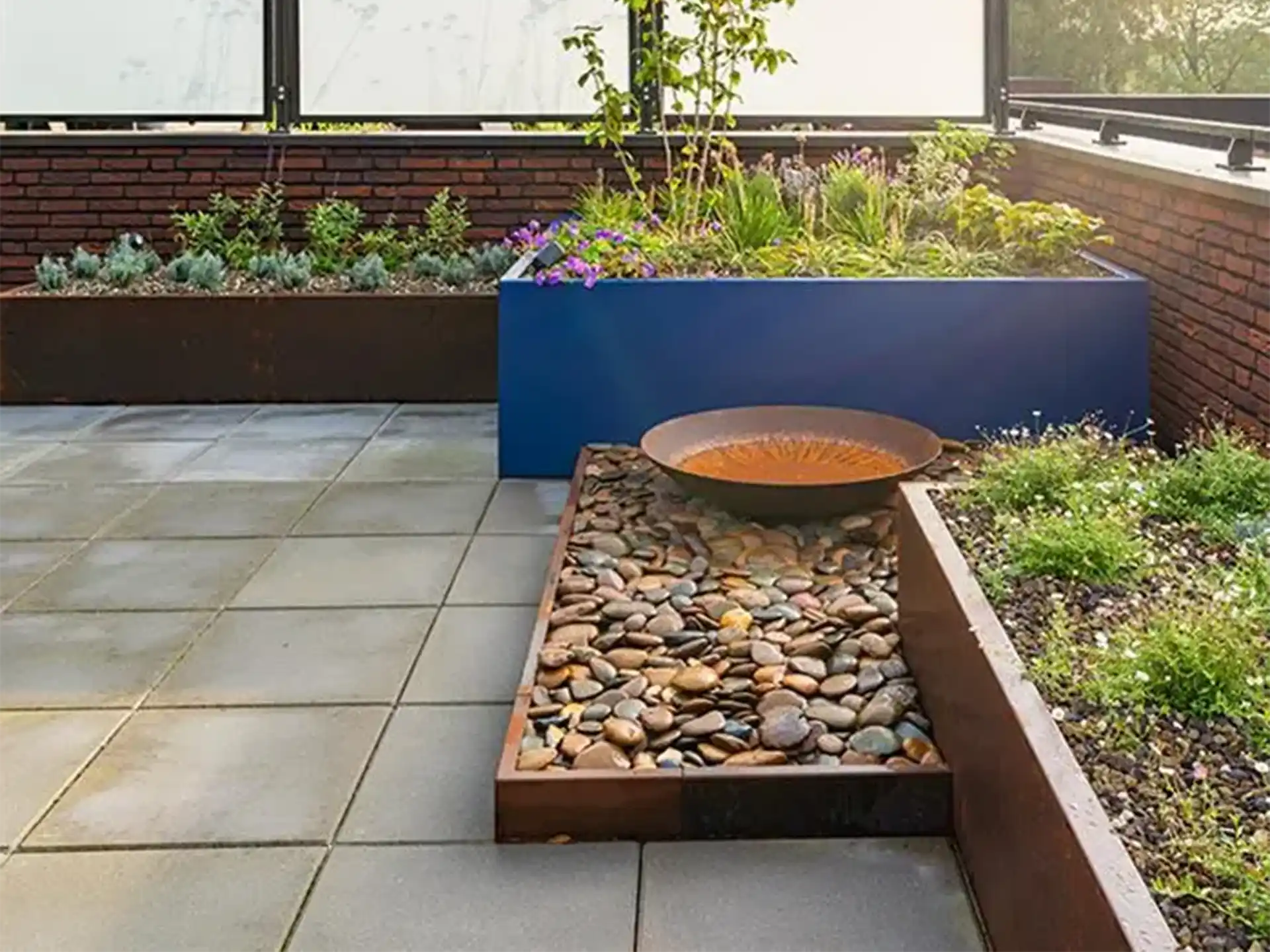 Adezz kantopsluiting van gezet cortenstaal toegepast langs een terras met beplanting en grind voor een moderne uitstraling.
