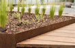 Adezz kantopsluiting van cortenstaal met rechte hoek, toegepast buiten langs een houten terras en plantenborder.