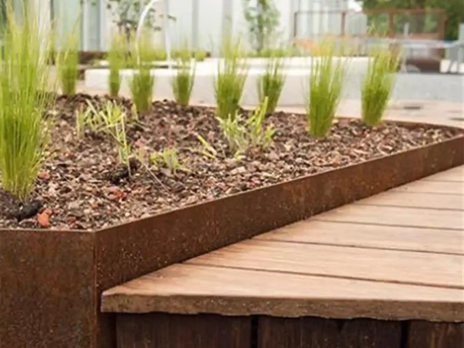 Adezz kantopsluiting van cortenstaal met rechte hoek, toegepast buiten langs een houten terras en plantenborder.