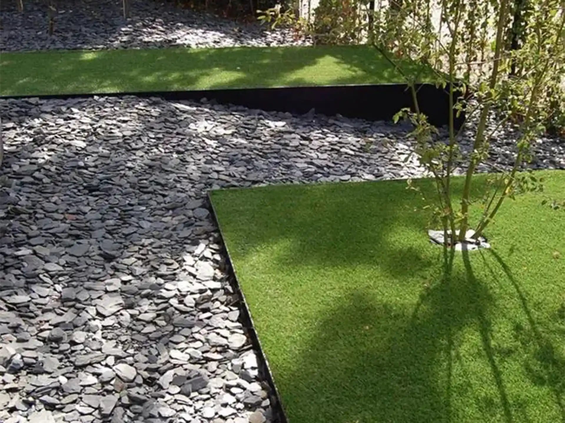 Adezz kantopsluiting van cortenstaal in hoekvorm, toegepast in een tuin met grind en kunstgras.