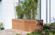 Adezz Malaga Rhombus hardhouten plantenbak, gevuld met bamboe en geplaatst op een modern terras tegen een houten wand.