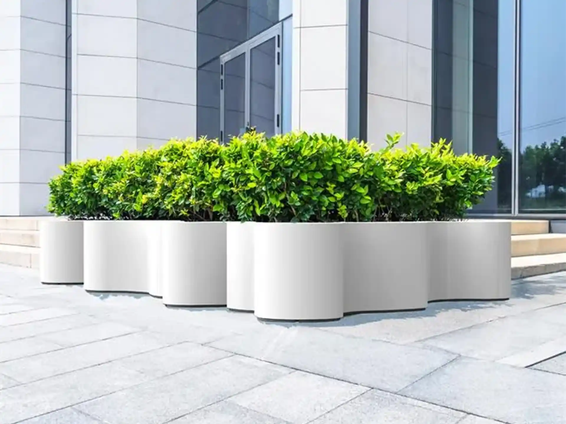 Adezz Organ polyester plantenbak rond organisch model in wit, geplaatst bij een moderne gevel met groene struiken.