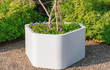 Adezz Shape polyester plantenbak rond hoeking model in wit, geplaatst in een tuin met grind en kleine boom.
