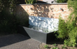 Adezz vijvermuur op aluminium vijver, modern rechthoekig design met waterval en pomp, geplaatst tegen een tuinmuur.