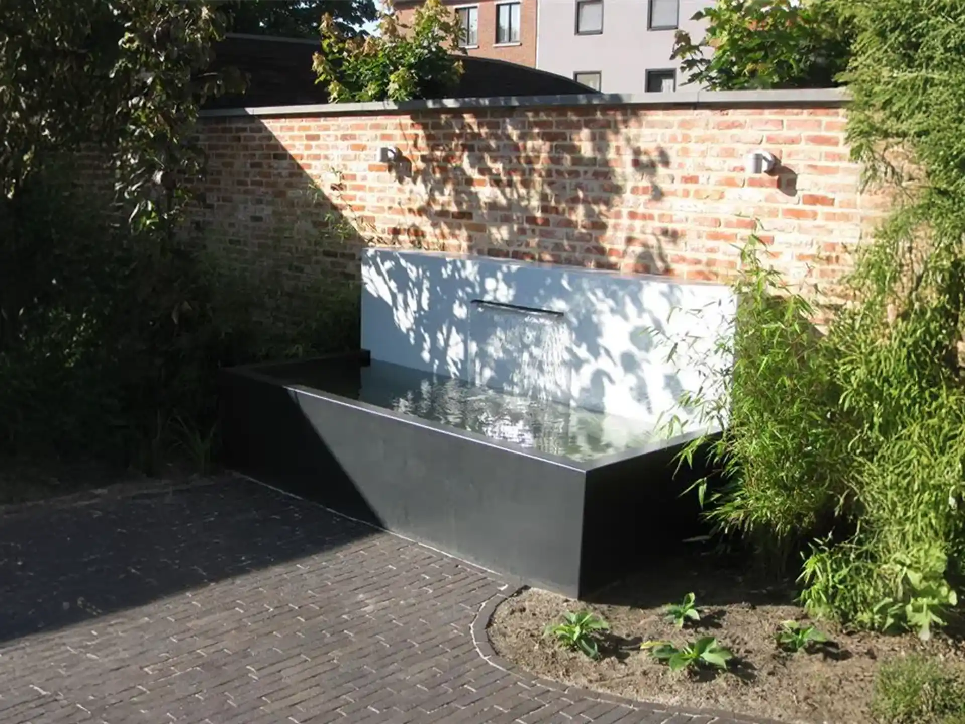 Adezz vijvermuur op aluminium vijver, modern rechthoekig design met waterval en pomp, geplaatst tegen een tuinmuur.