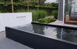 Adezz vijvermuur op aluminium vijver, moderne tuinopstelling met geïntegreerde waterval en pomp.