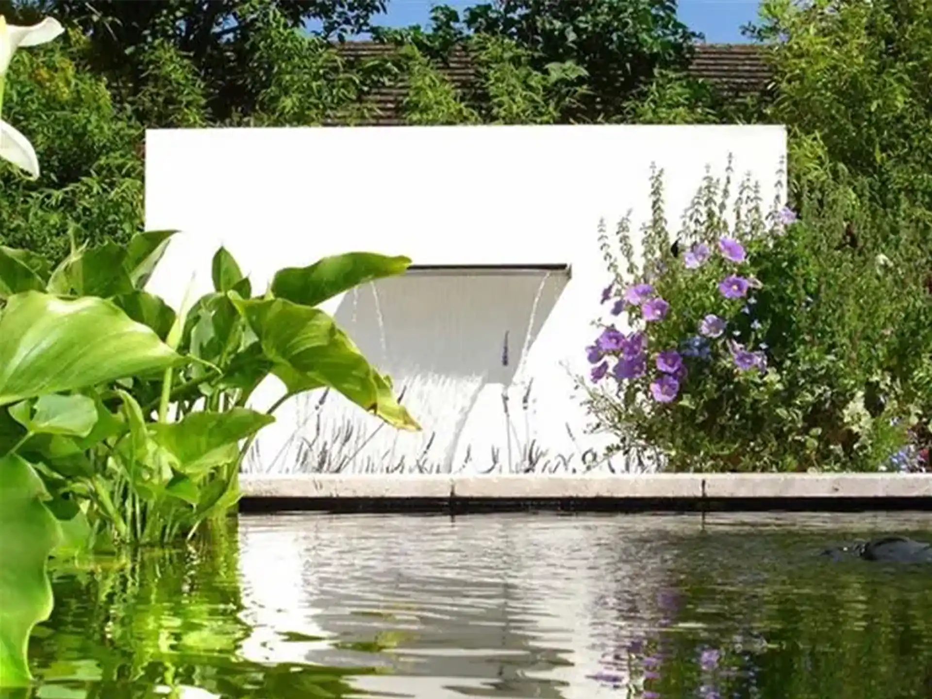 Adezz vijvermuur vrijstaand in aluminium uitvoering, met brede waterval en pomp, geplaatst in een groene tuin.