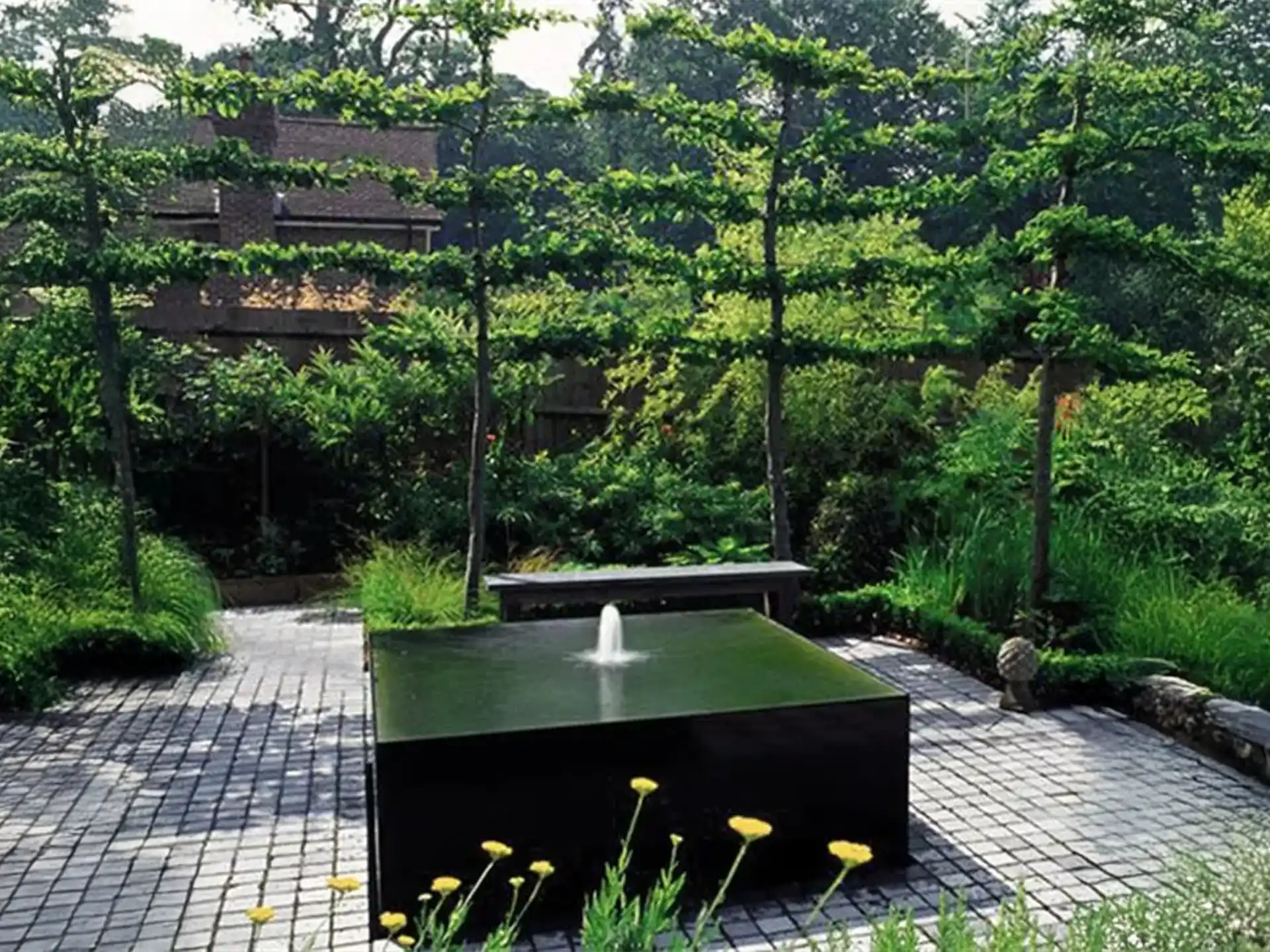 Adezz waterblok van aluminium met drie fonteinen, strak vormgegeven en geplaatst op een modern terras met groene tuinomgeving.