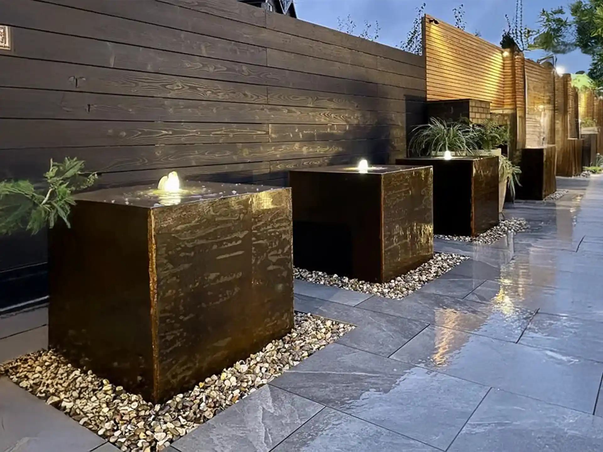 Cortenstaal waterblok van Adezz met drie fonteinen en LED-verlichting, stijlvol accent langs een terras in de avond.