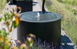 Close-up van Adezz ronde aluminium watertafel met fontein, water stroomt zacht in een strakke tuinomgeving.