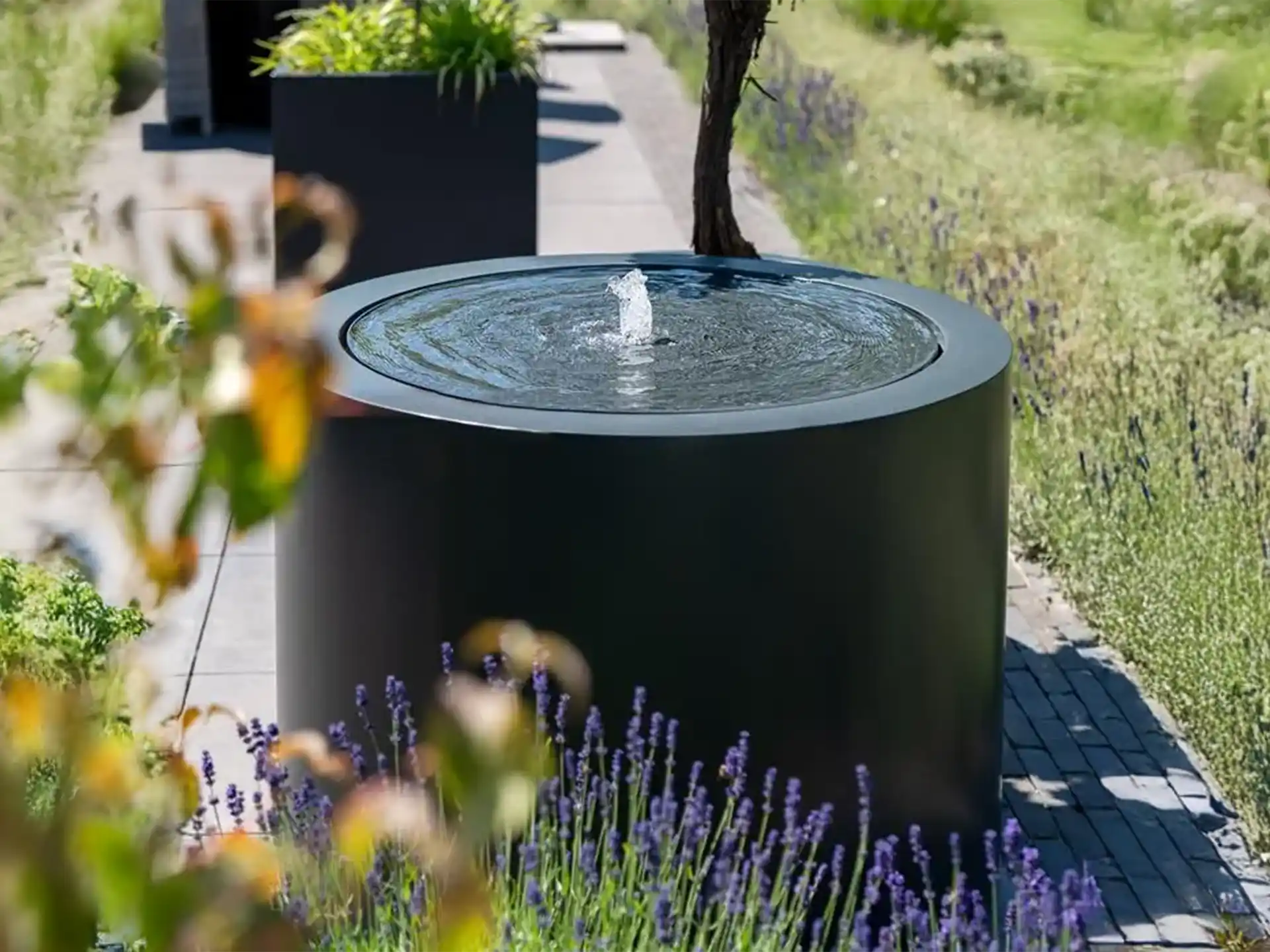 Close-up van Adezz ronde aluminium watertafel met fontein, water stroomt zacht in een strakke tuinomgeving.
