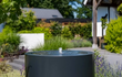 Adezz ronde aluminium watertafel met fontein, stijlvol geplaatst in een moderne tuin met beplanting.