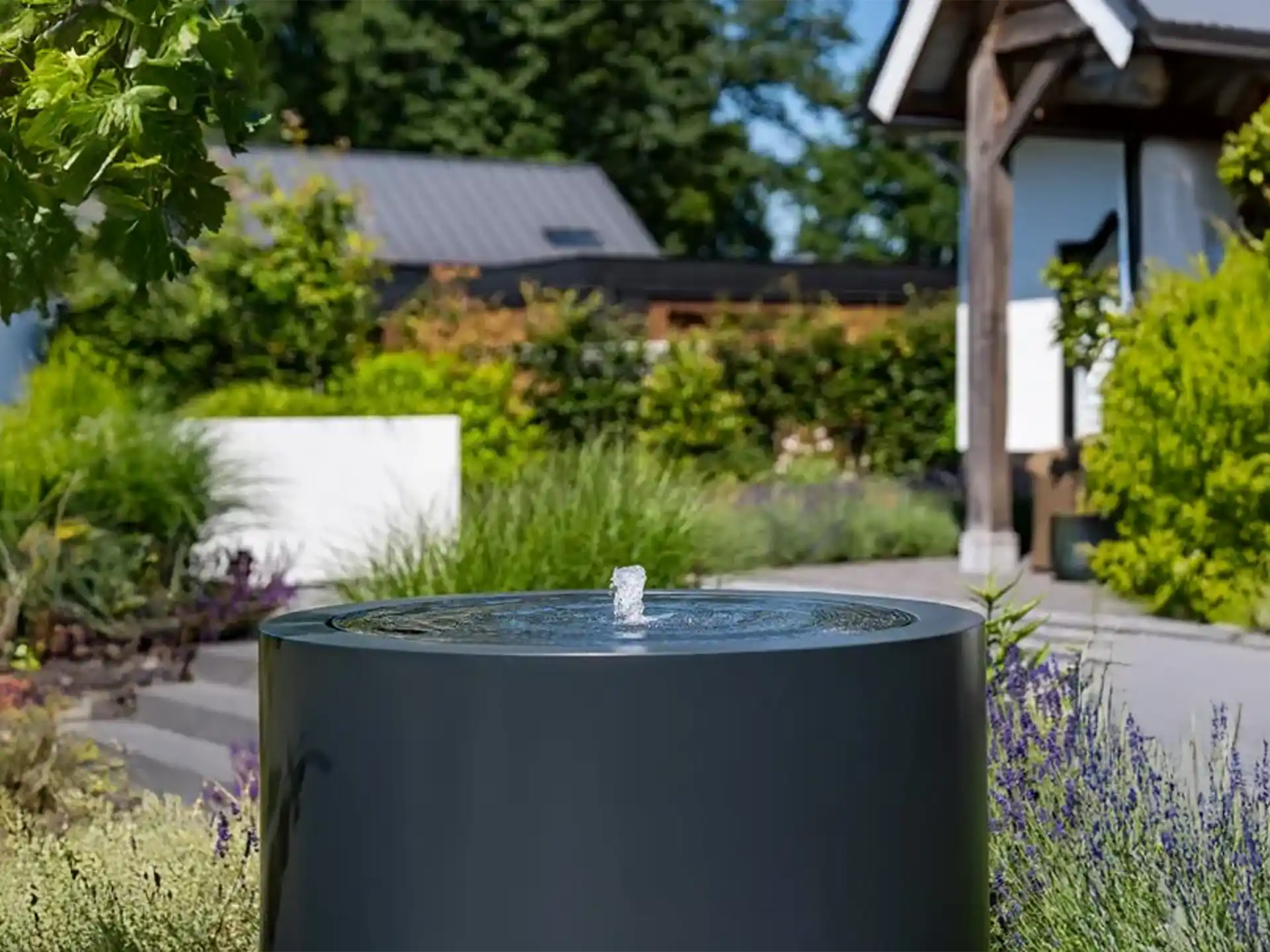 Adezz ronde aluminium watertafel met fontein, stijlvol geplaatst in een moderne tuin met beplanting.