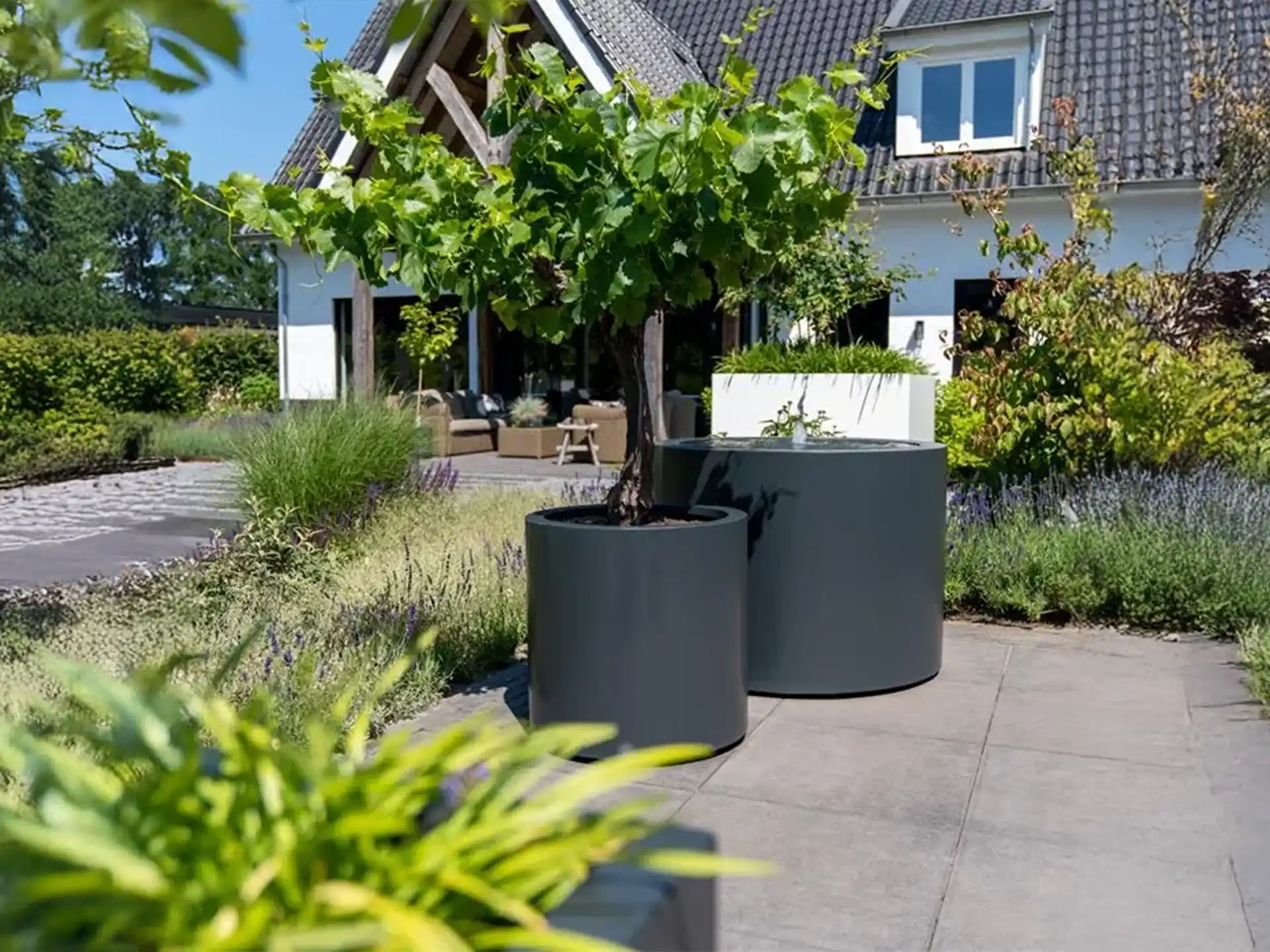 Een Adezz ronde aluminium watertafel met fontein in een ruime tuin bij een moderne woning.
