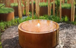 Adezz ronde watertafel van cortenstaal met fontein, geplaatst in een moderne tuin met natuurlijke uitstraling.