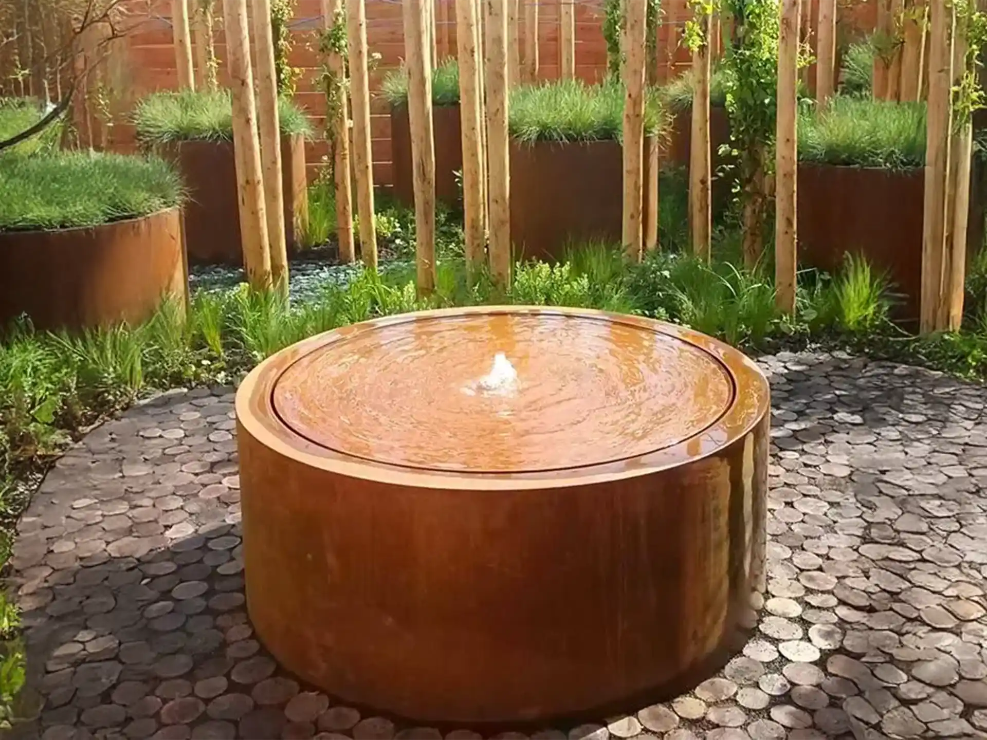 Adezz ronde watertafel van cortenstaal met fontein, geplaatst in een moderne tuin met natuurlijke uitstraling.