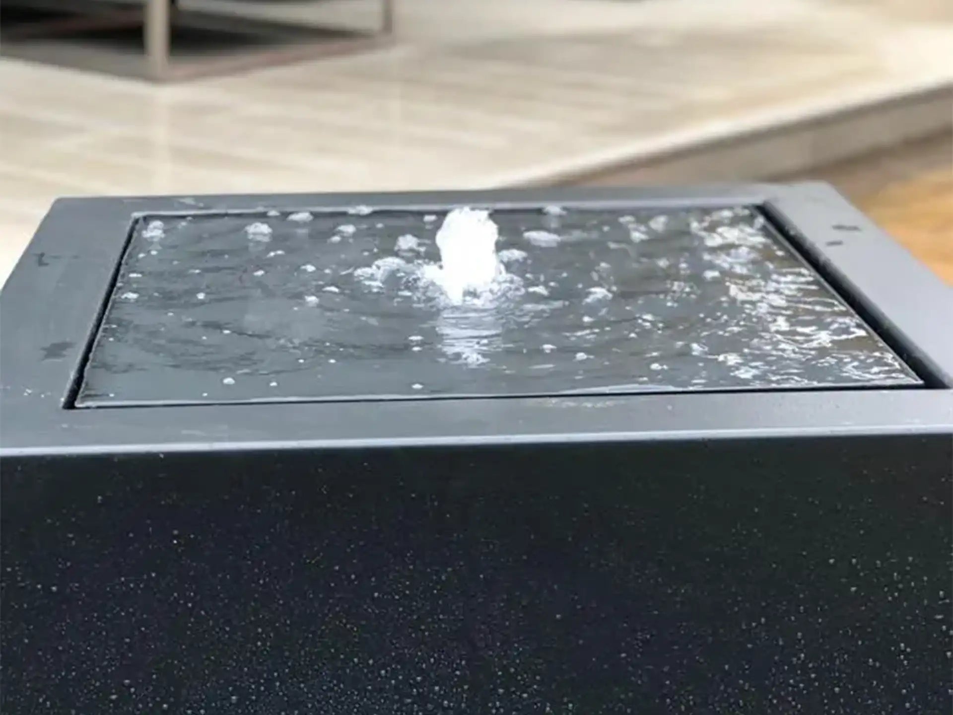 Close-up van aluminium Adezz watertafel in vierkante vorm met fontein die water omhoog spuit.