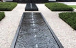 Aluminium Adezz watertafel in vierkante vorm met meerdere fonteinen, opgesteld in een moderne tuin met grind en strakke lijnen.
