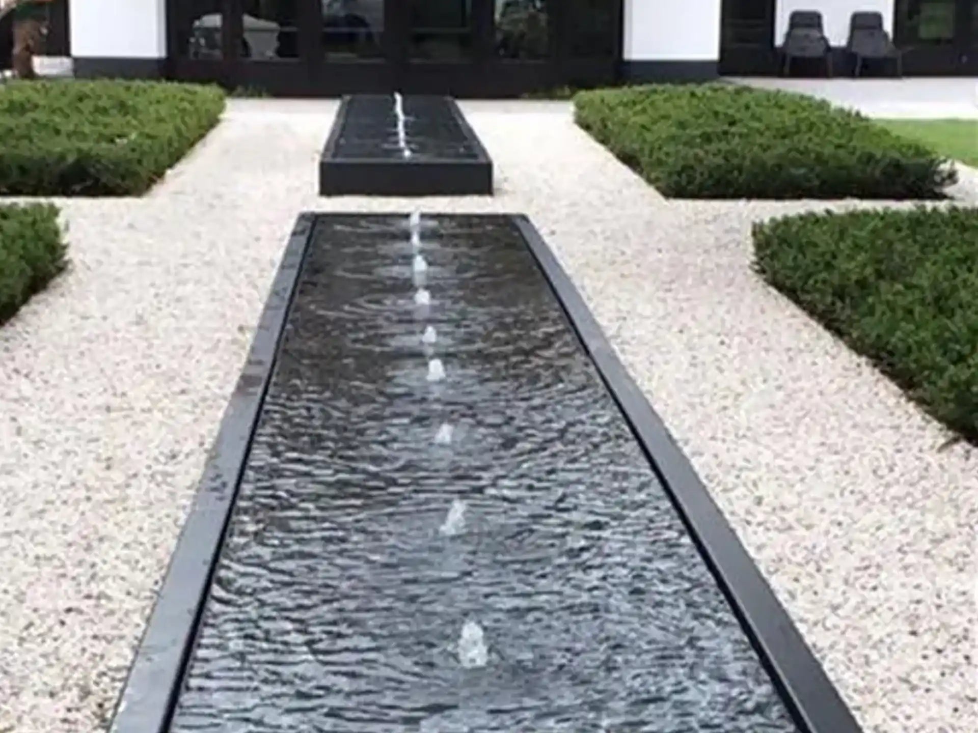 Aluminium Adezz watertafel in vierkante vorm met meerdere fonteinen, opgesteld in een moderne tuin met grind en strakke lijnen.
