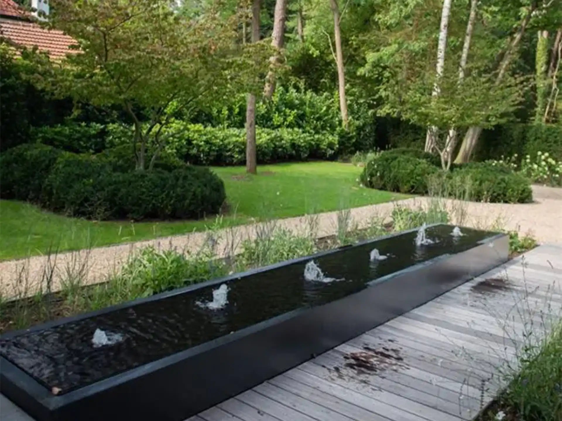 Adezz watertafel van aluminium in vierkante vorm met meerdere fonteinen, geplaatst in een moderne tuin met groen.