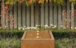 Adezz watertafel van cortenstaal in vierkant model met fontein, geplaatst in een tuin met groene beplanting.