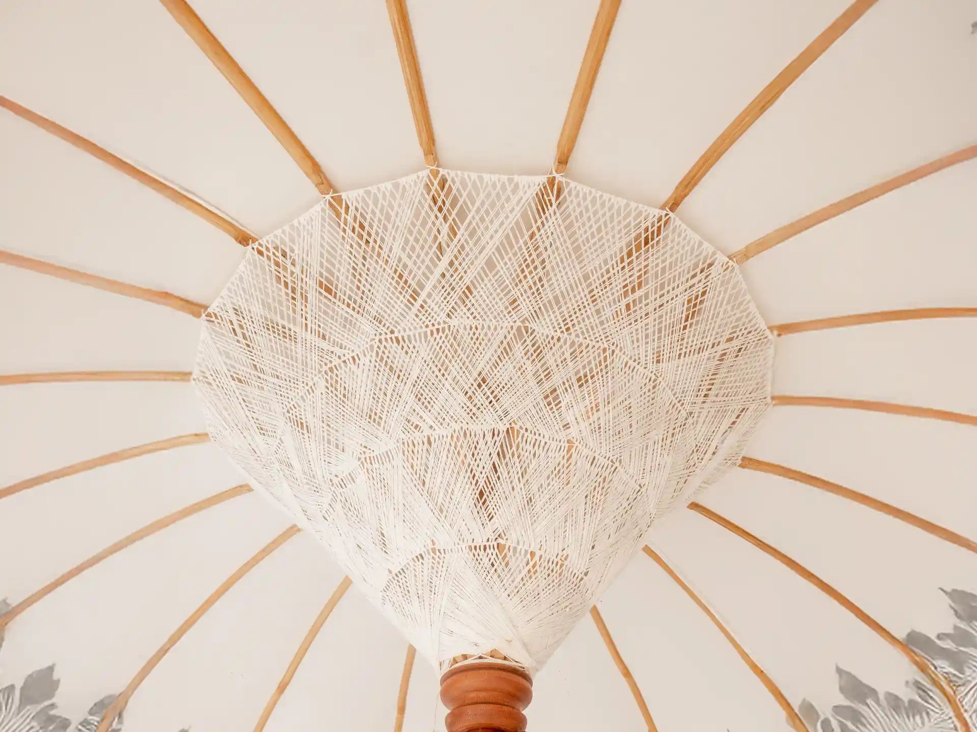 Detailopname van de binnenkant van een Balinese crème parasol met half zilveren beschildering en traditionele houten constructie.