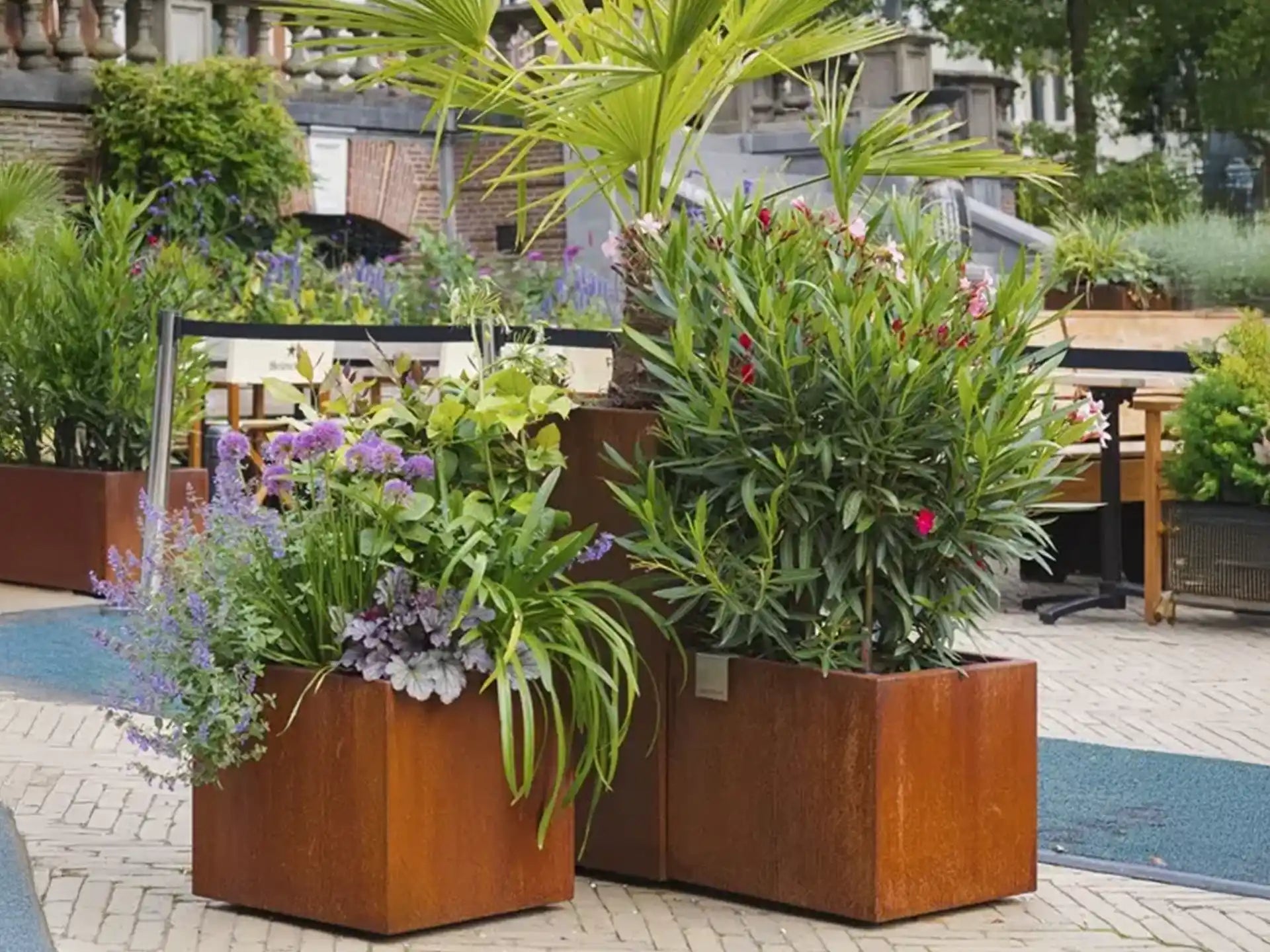 Rechthoekige Adezz Carrez Cortenstaal Plantenbak met wielen gevuld met kleurrijke bloemen en planten op een terras.