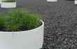 Witte Adezz Circum aluminium plantenbak zonder bodem gevuld met siergras op een dakterras met grind.