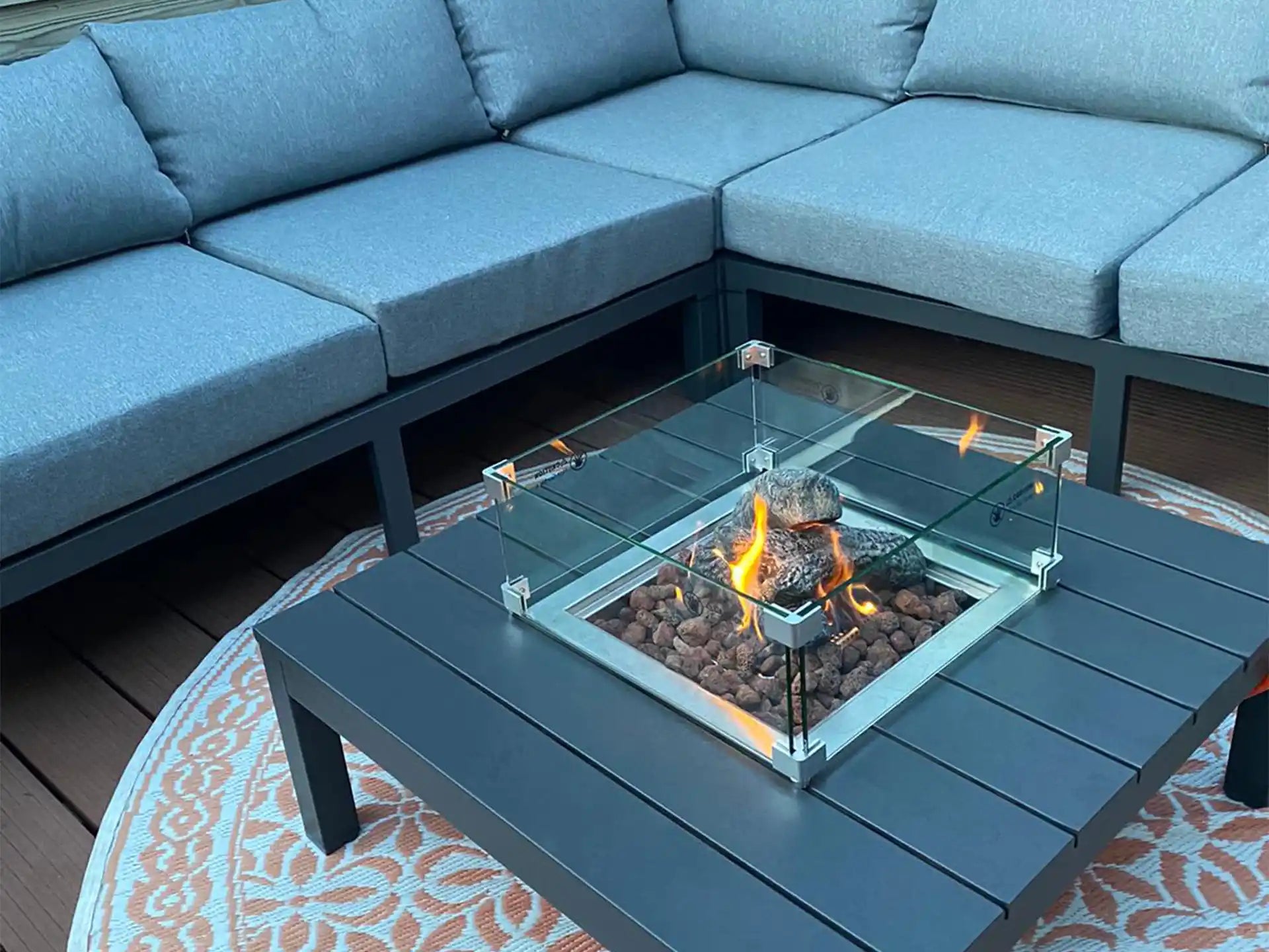 Gofire glasombouw 40 × 40 cm geplaatst in een loungeset met brandende haard, ideaal voor sfeervolle buitenruimtes.