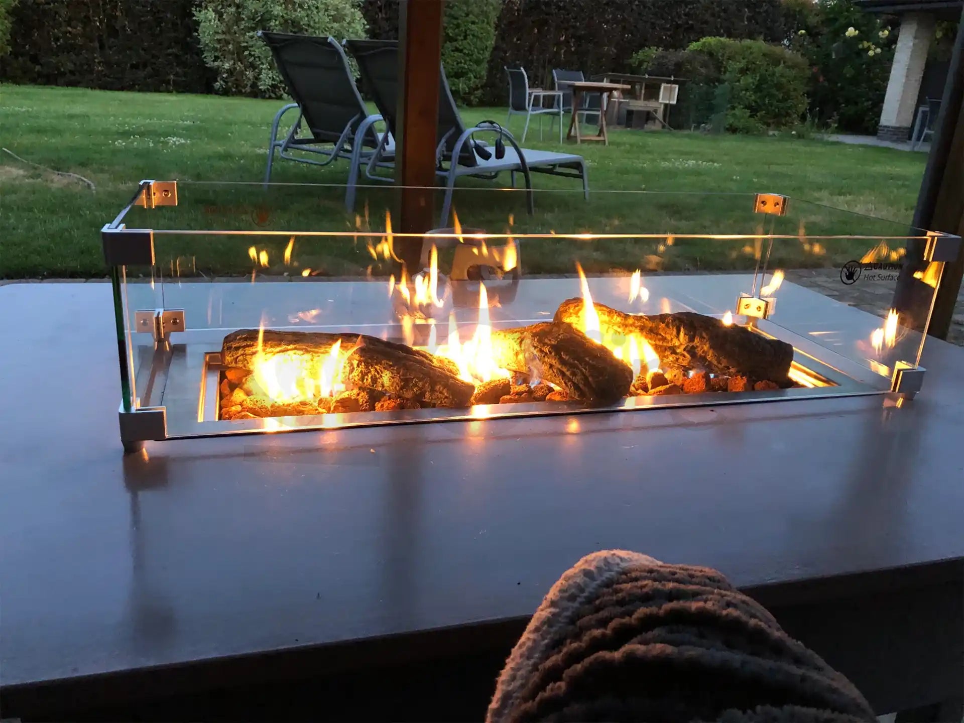 Sfeervolle terrasopstelling met Gofire keramische houtblokken in een glazen tafelhaard, brandend in een moderne buitenomgeving.