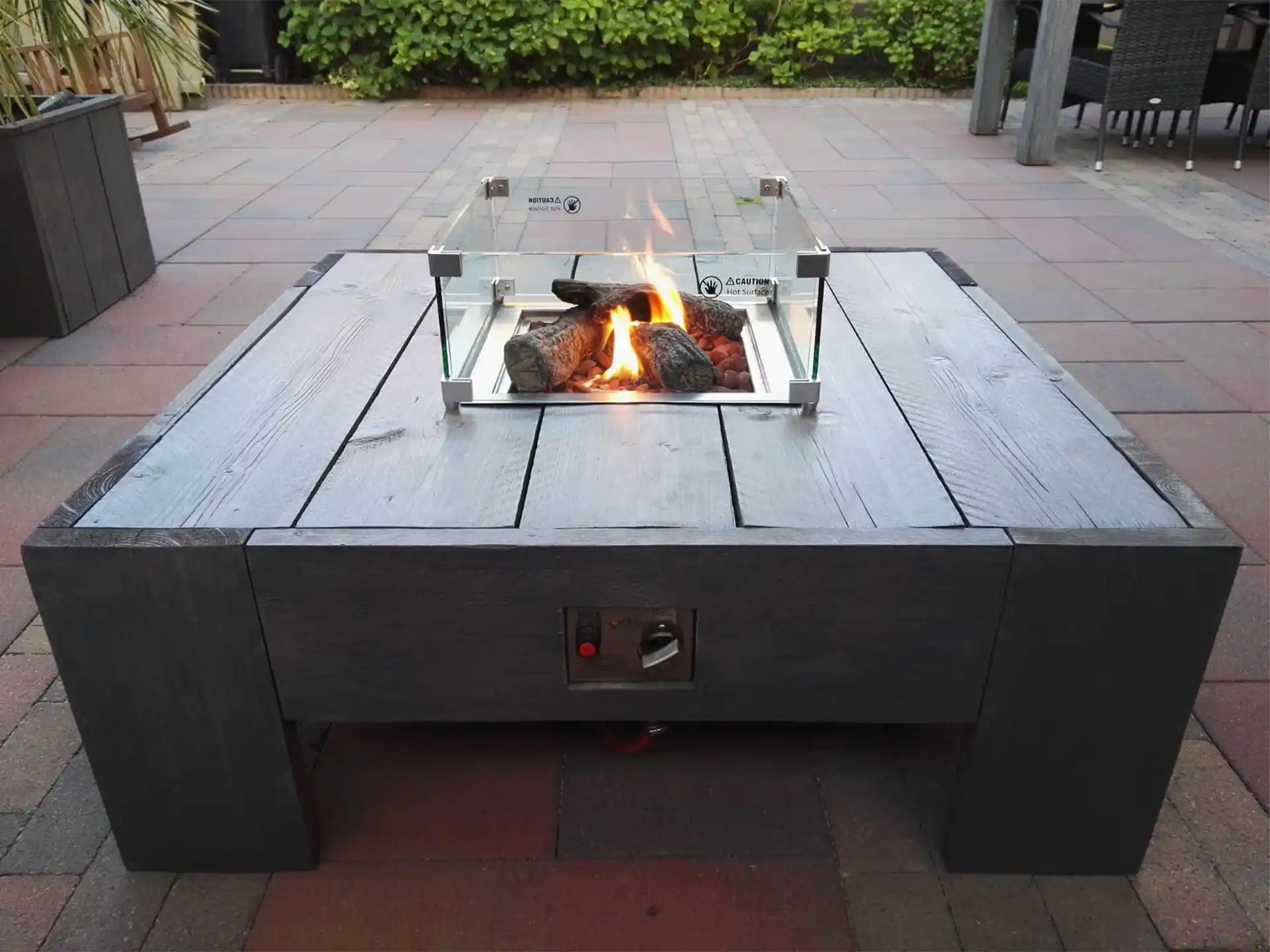 Vierkante Gofire inbouwbrander met glasombouw geïntegreerd in houten tafel, brandend op een terras in daglicht.