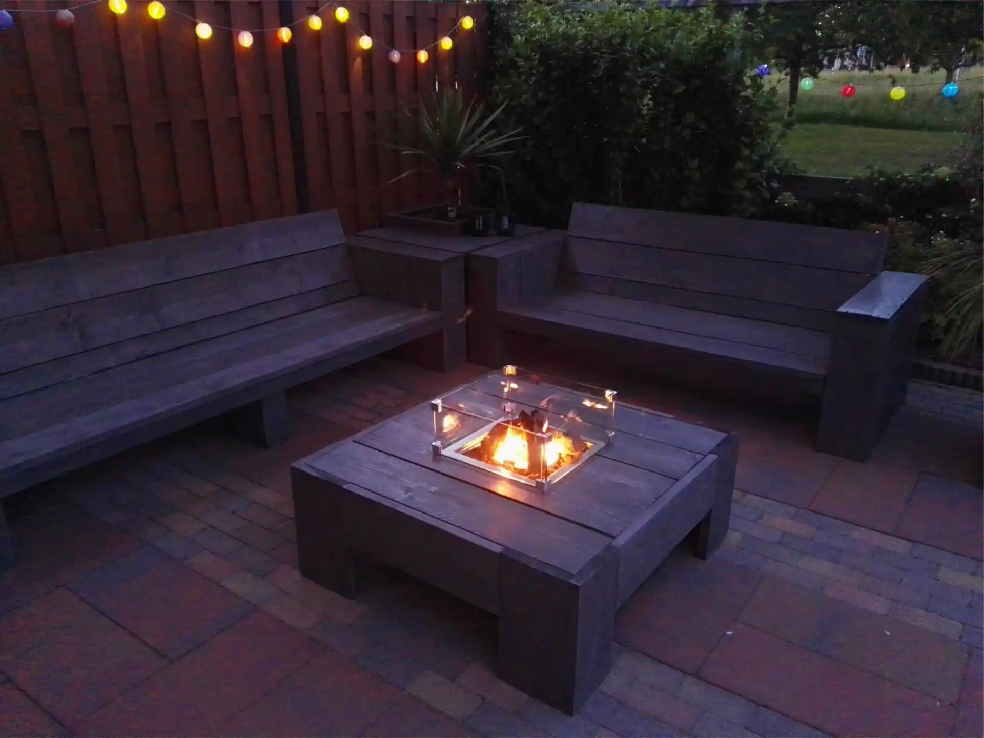 Gofire inbouwbrander 40 × 40 cm brandend in houten vuurtafel in een sfeervolle tuinsetting met buitenverlichting.