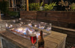 Gofire inbouwbrander 75 × 25 cm brandend in houten vuurtafel met glasombouw, sfeervol terras met drankjes en planten.