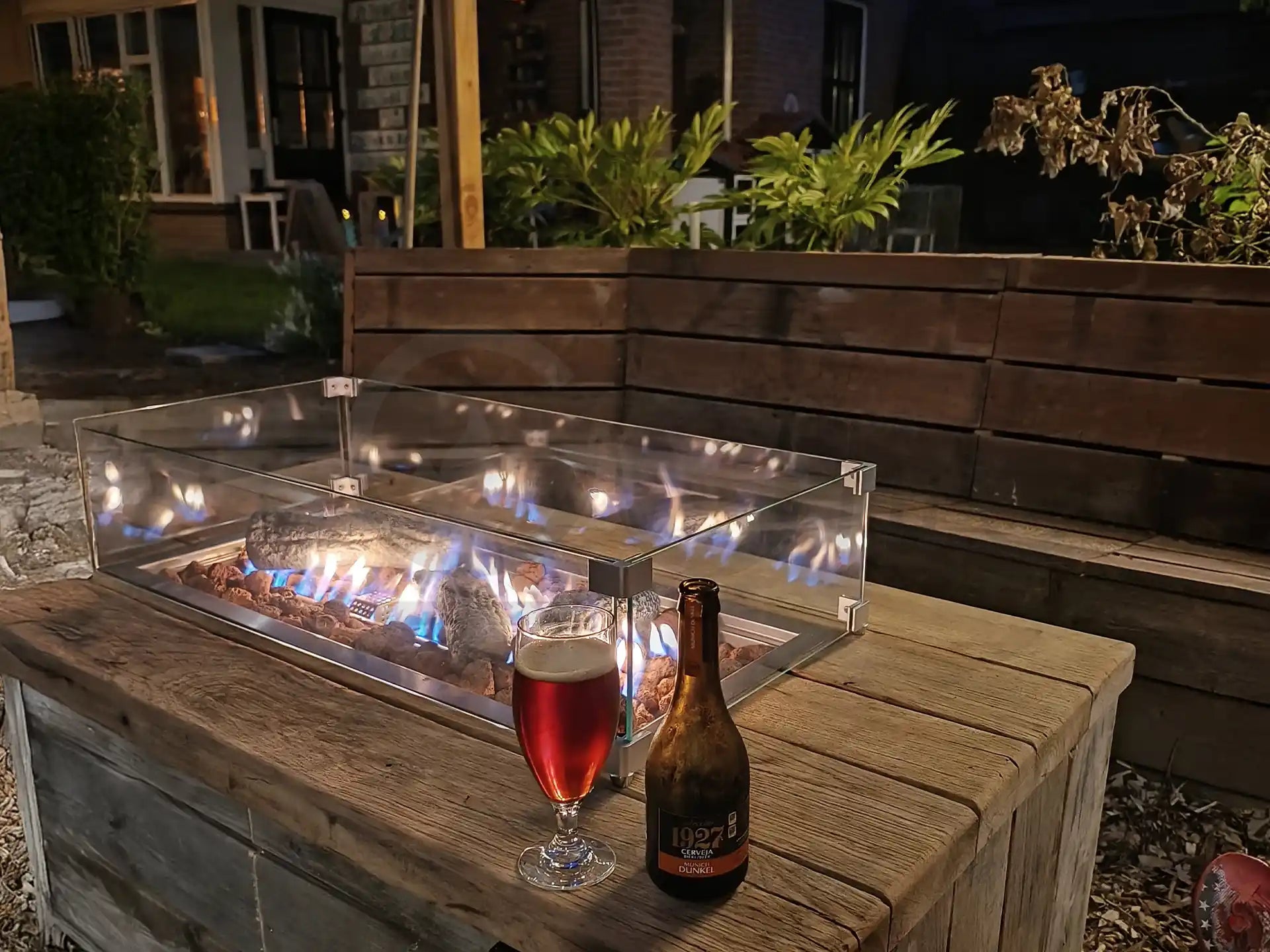 Gofire inbouwbrander 75 × 25 cm brandend in houten vuurtafel met glasombouw, sfeervol terras met drankjes en planten.