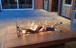 ofire inbouwbrander 75 × 25 cm geplaatst in een strakke houten vuurtafel met vlammenspel op een terras in de avond.