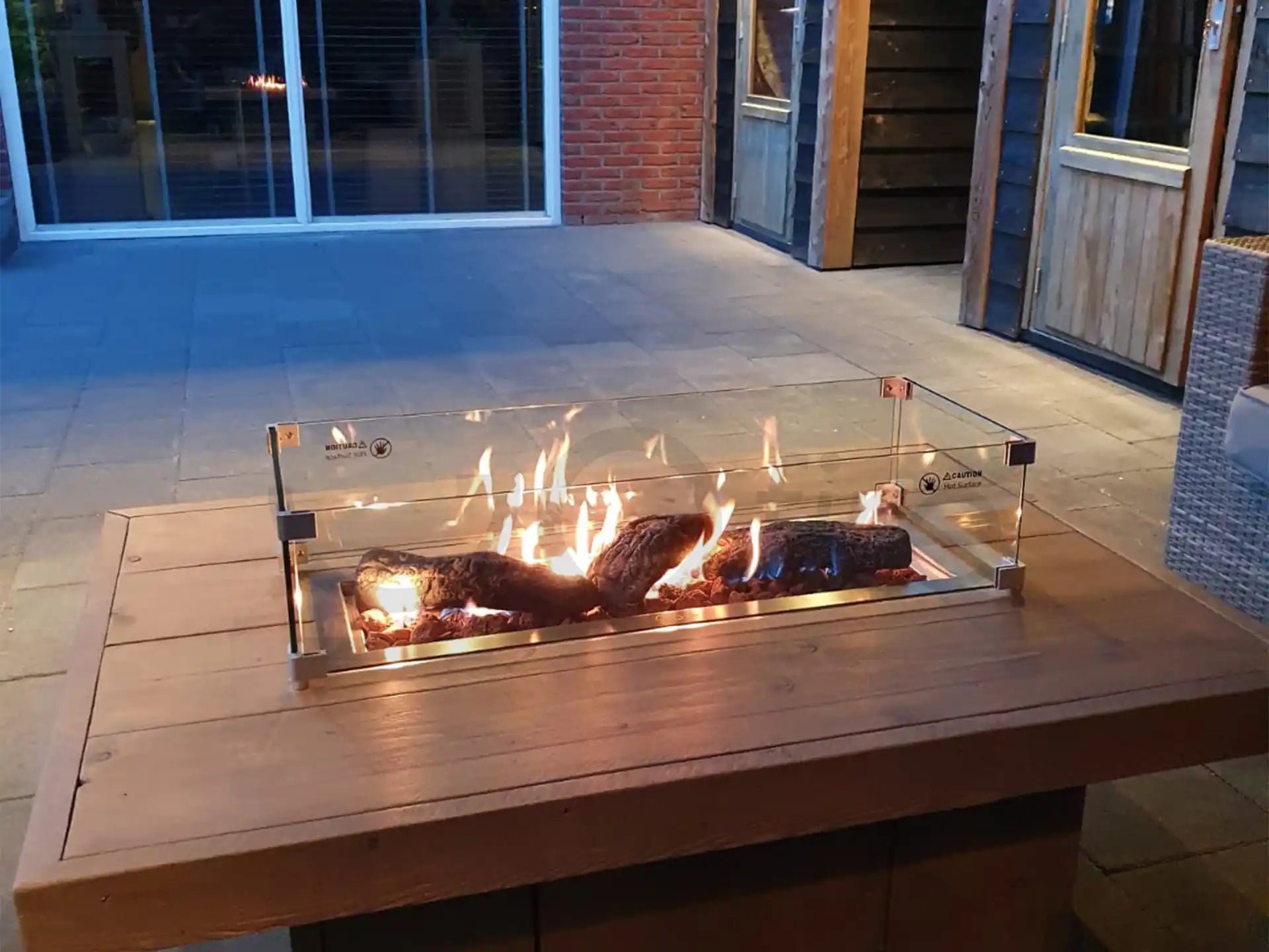 ofire inbouwbrander 75 × 25 cm geplaatst in een strakke houten vuurtafel met vlammenspel op een terras in de avond.