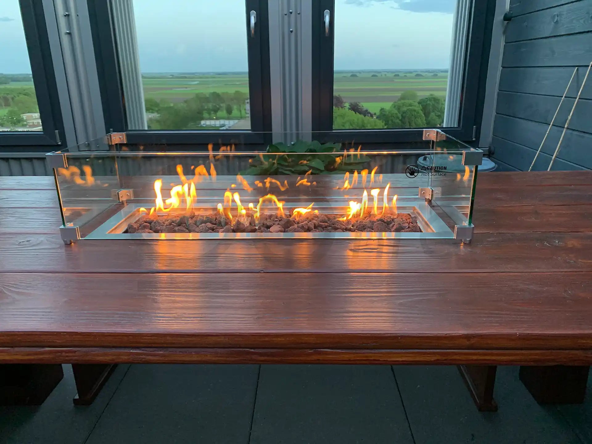 Gofire inbouwbrander 75 × 25 cm met glasombouw, geplaatst op houten tafel met panoramisch uitzicht, vlammen sfeervol brandend.