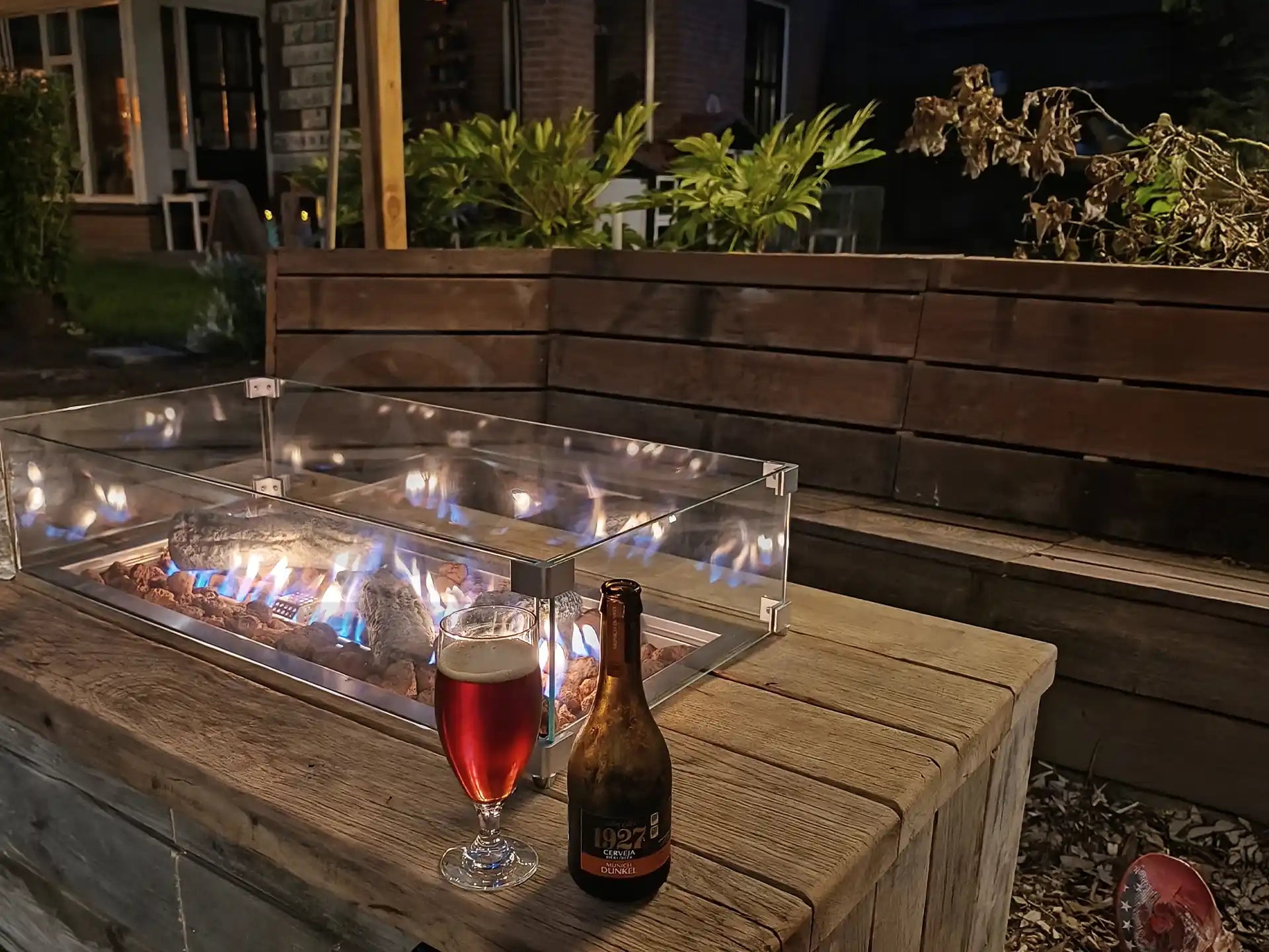  Gofire inbouwbrander 79 × 36 cm brandend in houten vuurtafel met glasombouw, sfeervol terras met drankjes en planten.
